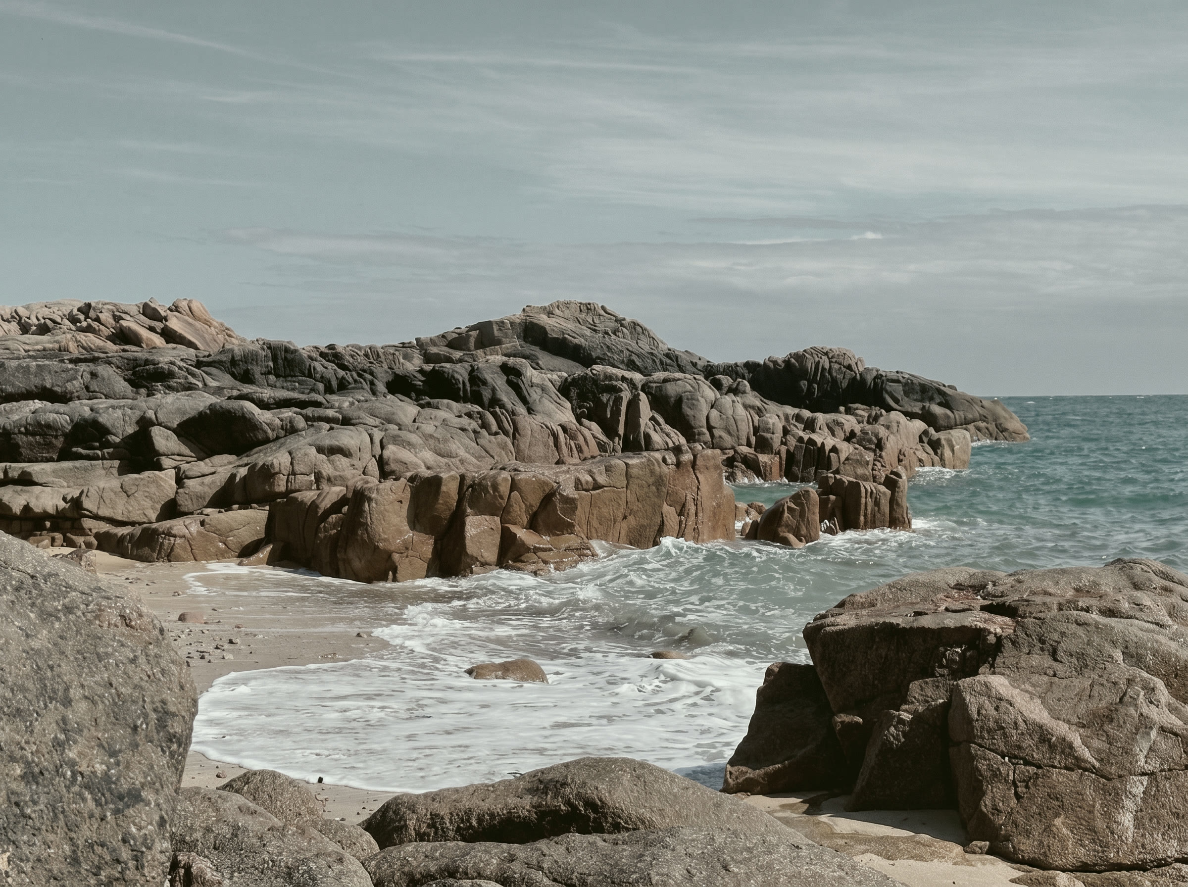 Granite headland and calm sea on the Jersey coast in grey morning light